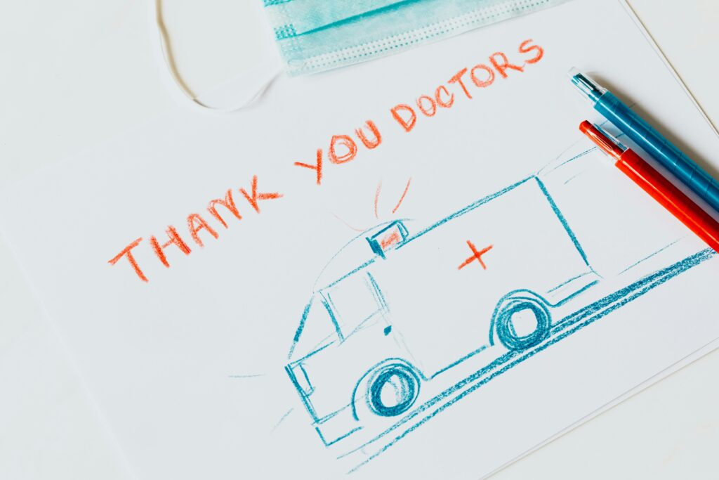 Handcrafted drawing of an ambulance expressing gratitude to doctors, accompanied by a face mask and colored pencils.